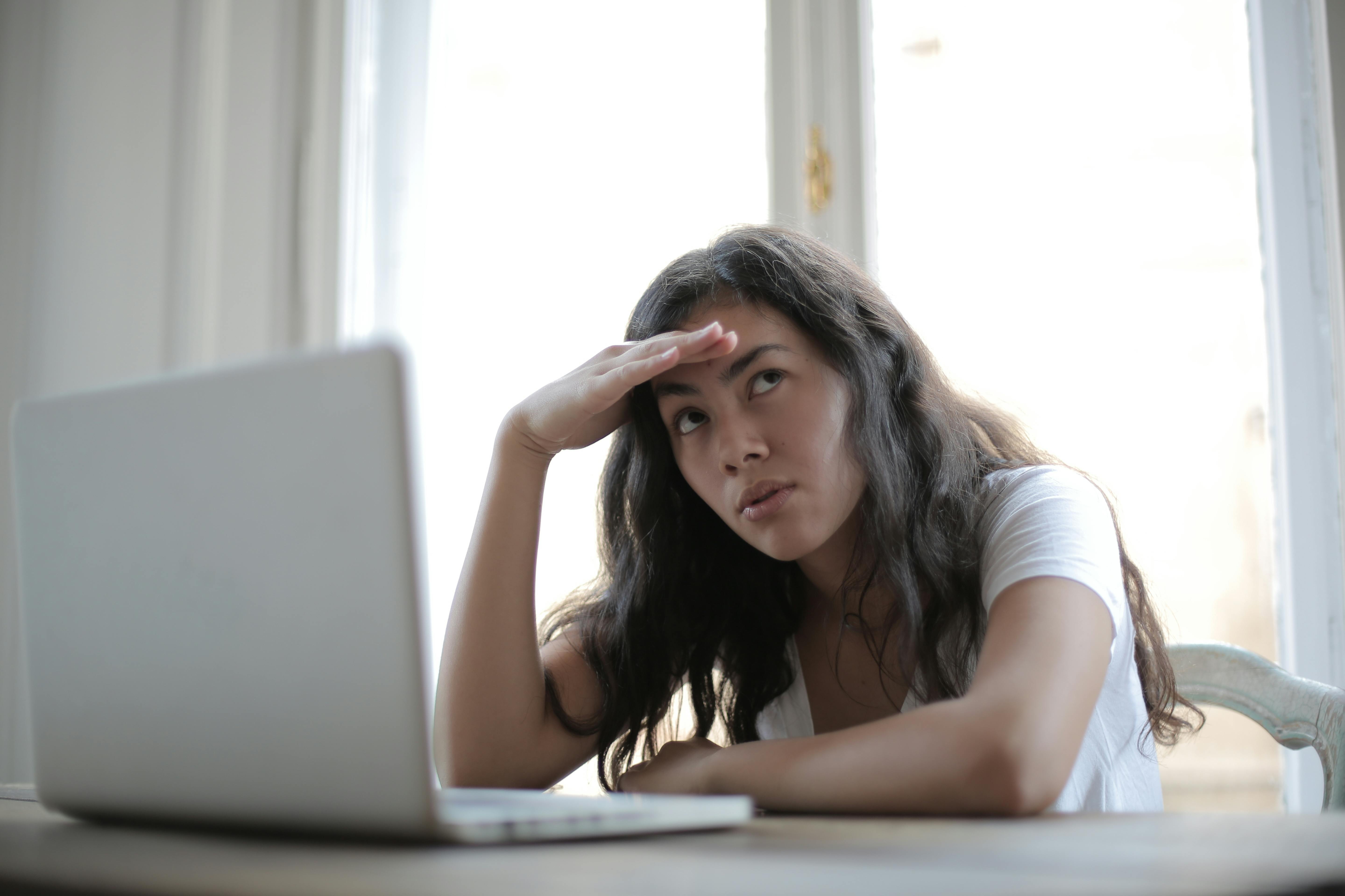 Een vrouw zit achter een bureau en kijkt peinzend naar zijn laptop.